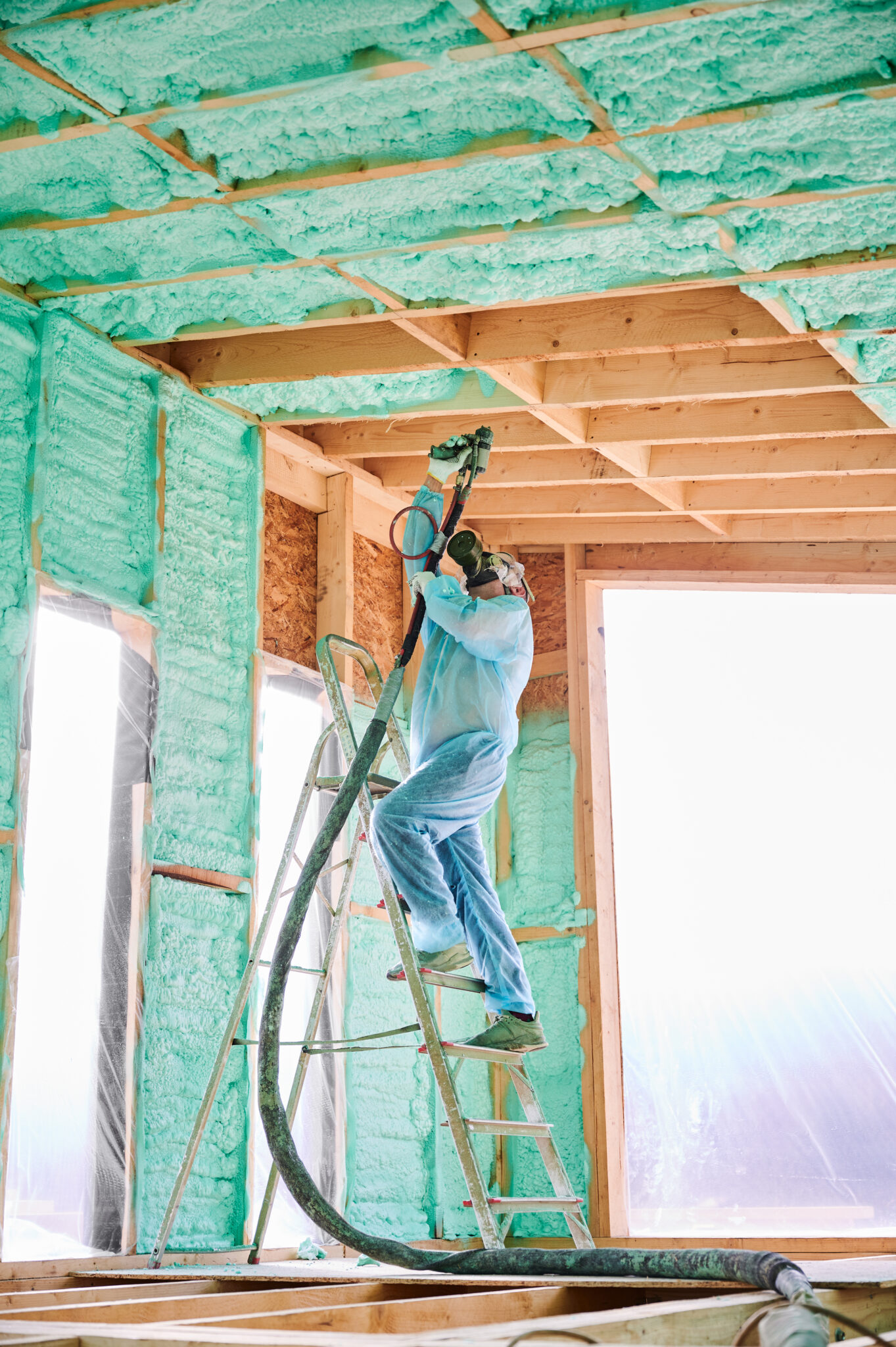 Male builder insulating wooden frame house. Man worker spraying polyurethane foam inside of future cottage, using plural component gun. Construction and insulation concept.