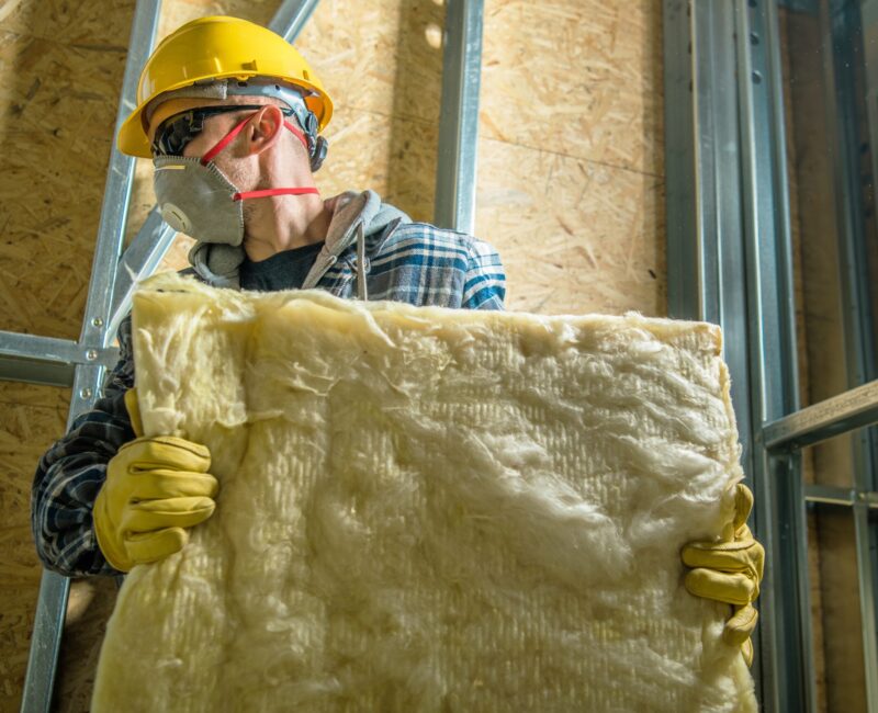 Caucasian Construction Worker Wearing Safety Mask Moving Pieces of Mineral Wool Insulation.